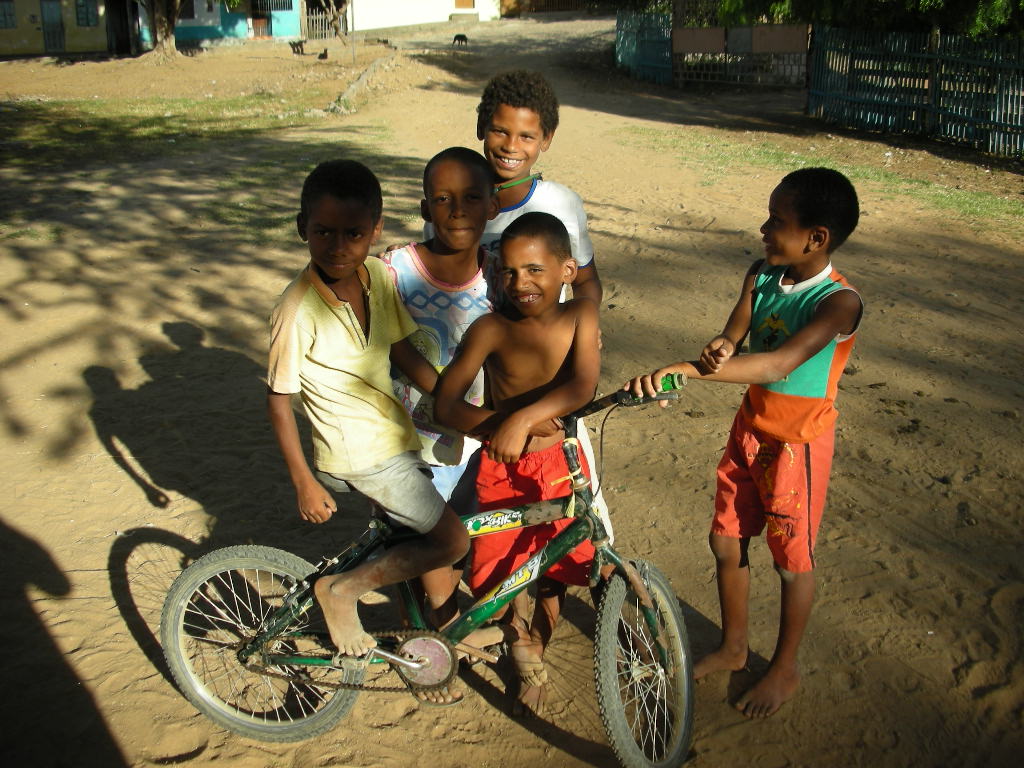 Brasilianische Kinder posieren lächelnd mit schmutzigen Füßen auf einem Mountainbike im Sand