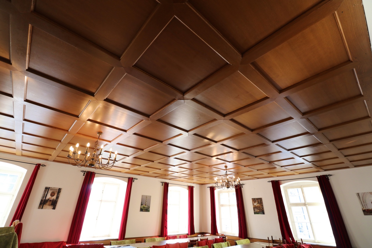 Blick über die festliche Bestuhlung rauf auf die quadratische Holzdecke mit ihren schicken Kronleuchter