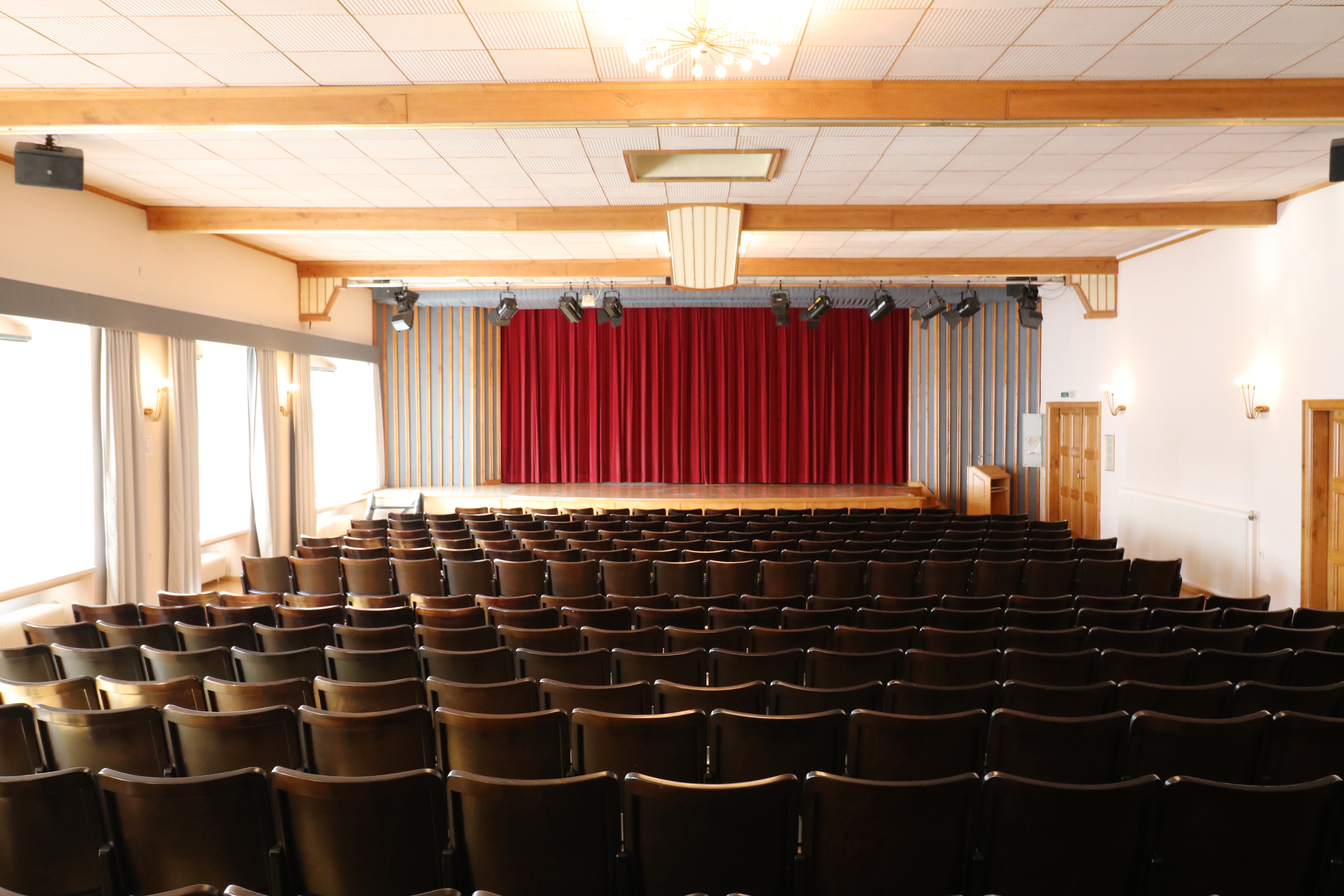 Ein großer Theatersaal mit dunkelbrauner Holzbestuhlung mit Blick in Richtung zugezogenem roten Bühnenvorhang