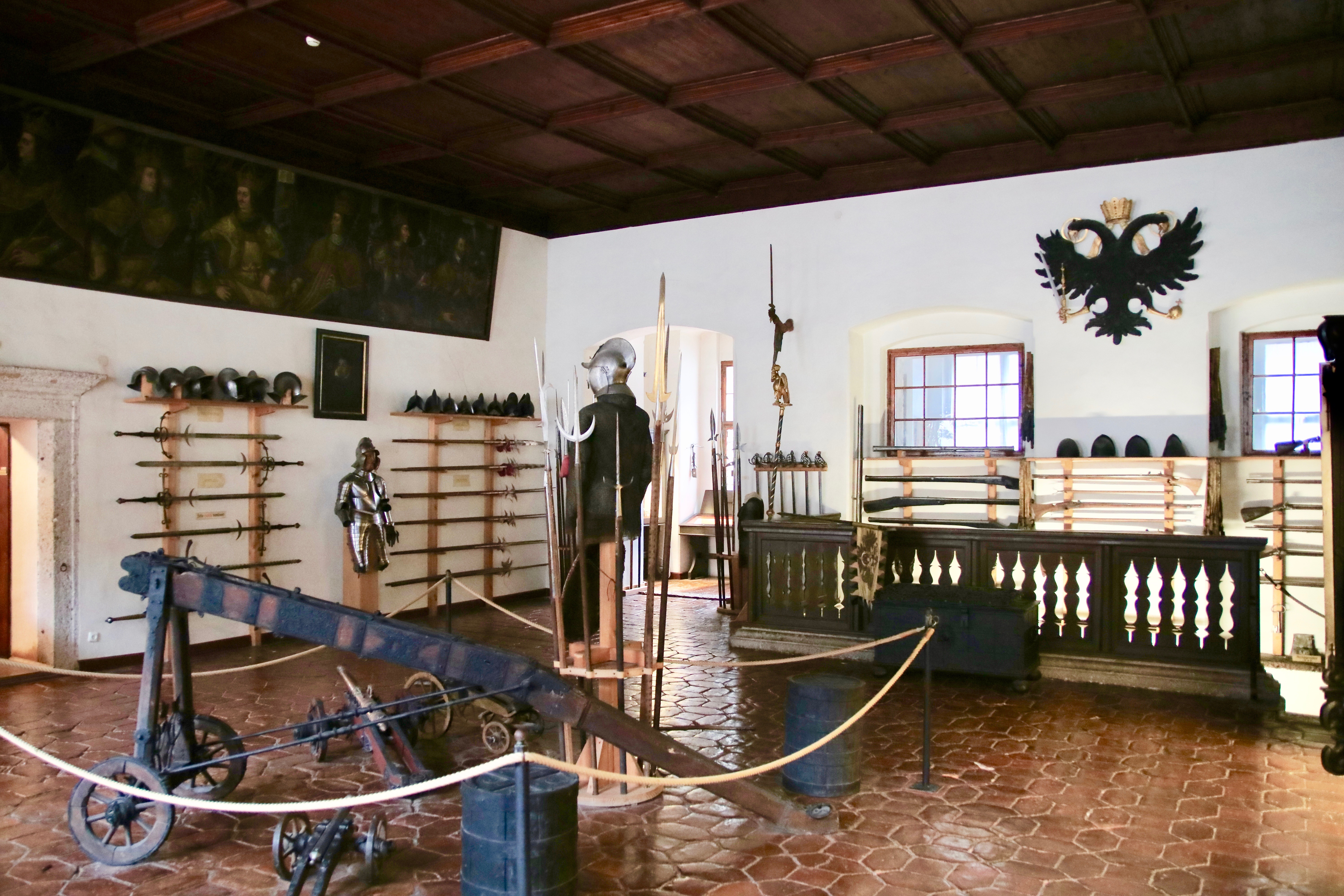 Mittelalterliche Gegenstände, wie Waffen und eine Ritterrüstung, in einem Raum mit dunkler Holzdecke