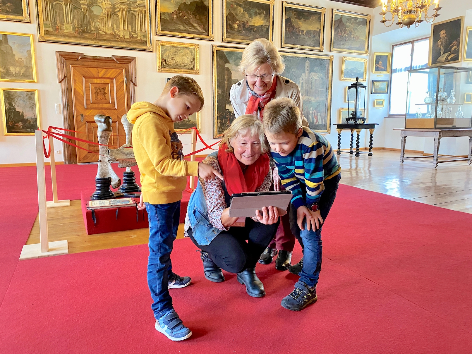 Zwei Kinder machen eine Stiftstour mit deren Omas, sie blicken alle auf ein Tablet und rätseln gemeinsam