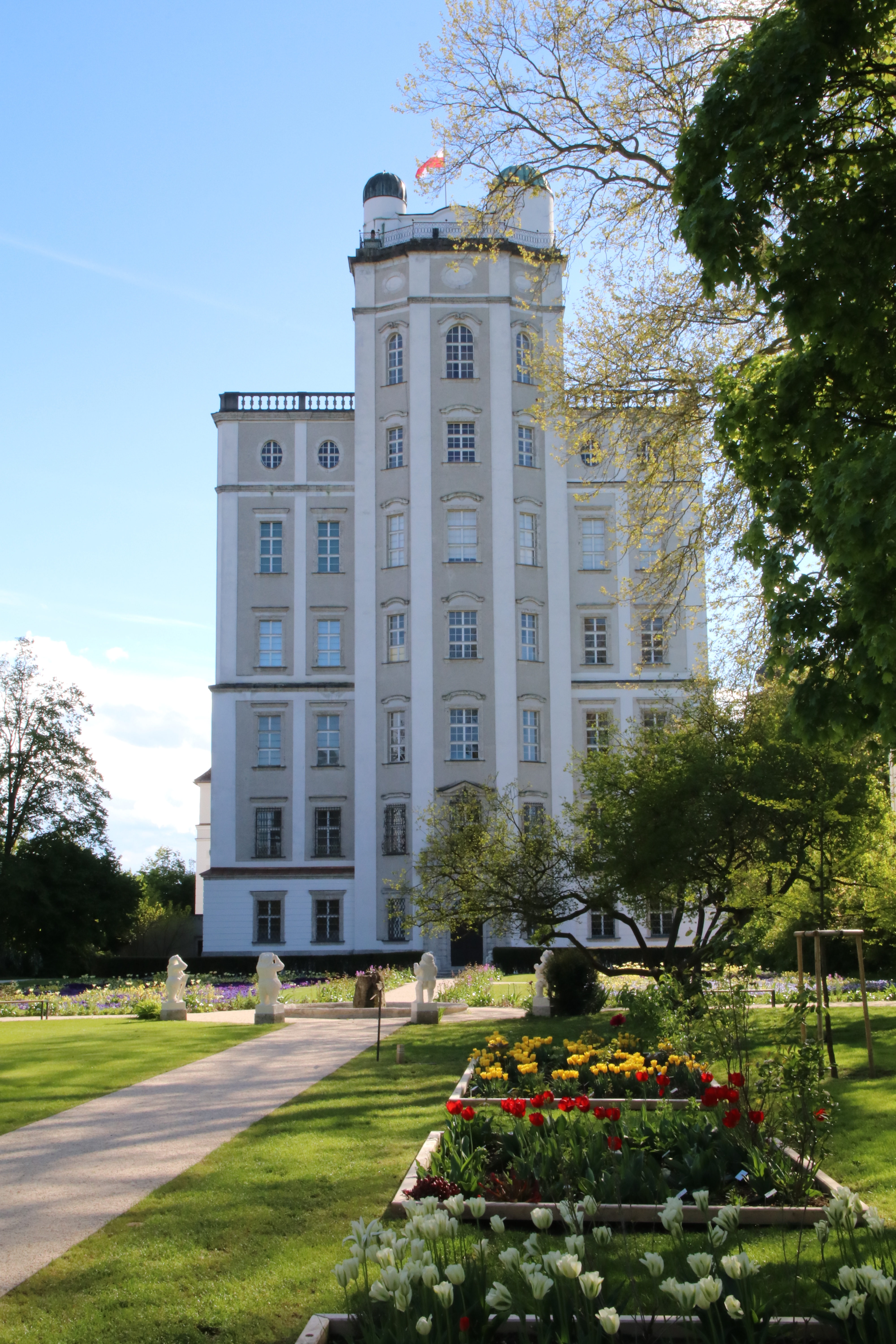 Ein heller Kiesweg führt zur Sternwarte. Daneben befinden sich quadratisch angelegte Blumenbeete, in jeweils einheitlichen Farben.