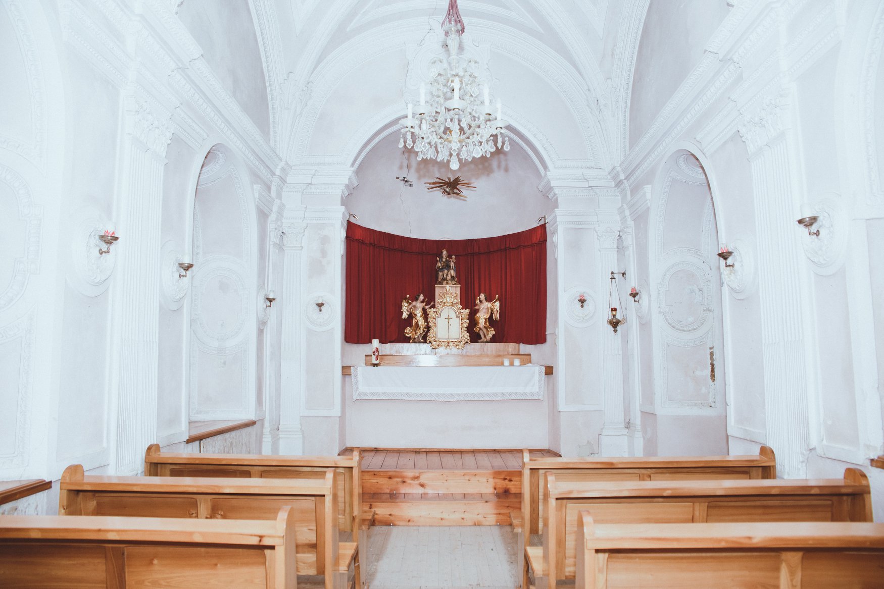 Pernsteiner Marienkapelle: Klarweiße Wände, frische Holzbänke und ein heller Altar mit Goldfiguren und im Hintergrund einem roten Samtvorhang.