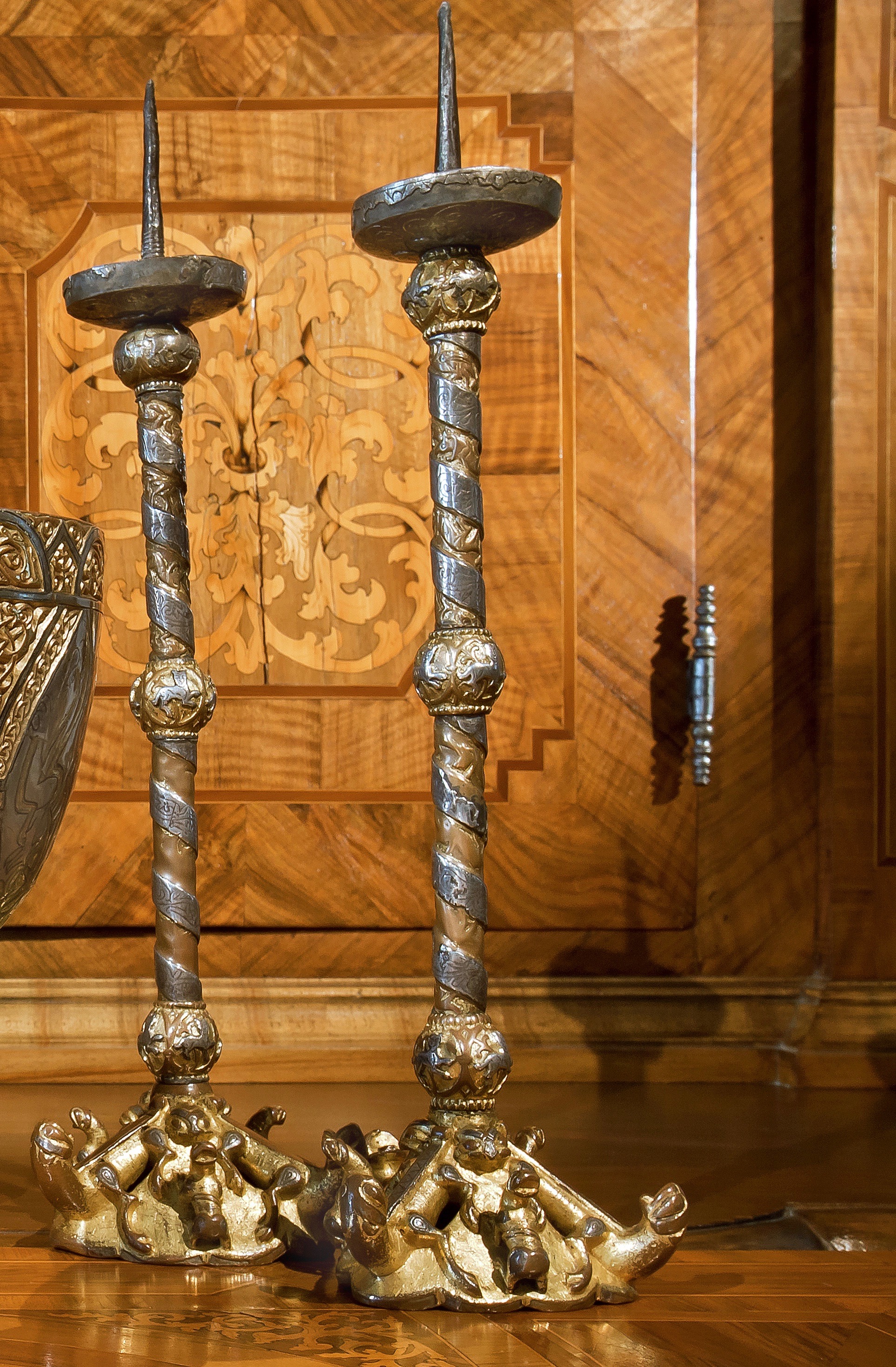 Zwei Leuchter aus Silber und Gold: große starkverzierte Standfüße, mit Silber umwundene Schaftteile mit drei gleichverteilten Kugelelementen, oben die funktionalen Aufsätze inklusive der Spieße für die Kerzen