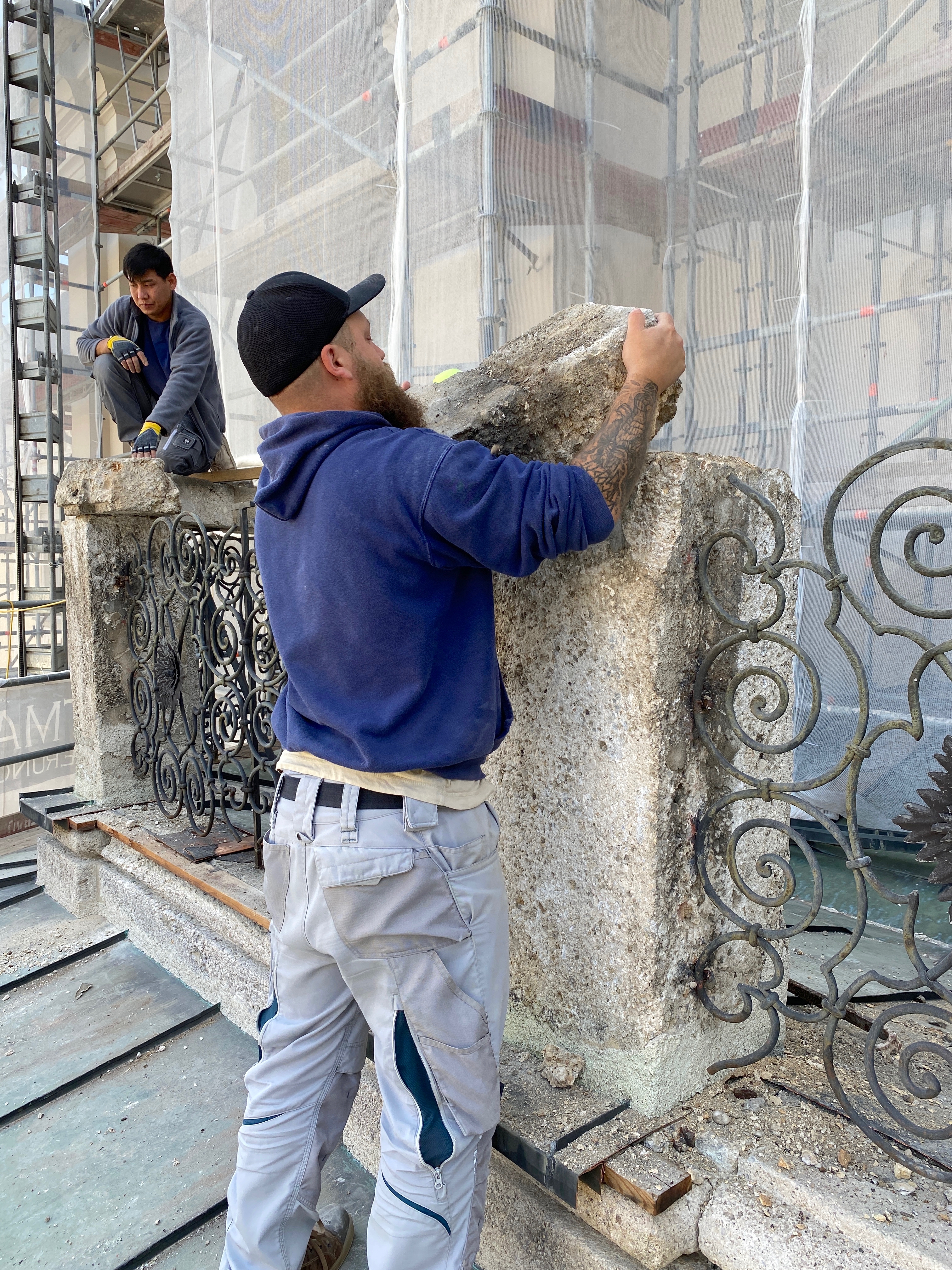 Ein Bauarbeiter hebt einen großen Steinblock von dem Fassadengeländer der Stiftskirche
