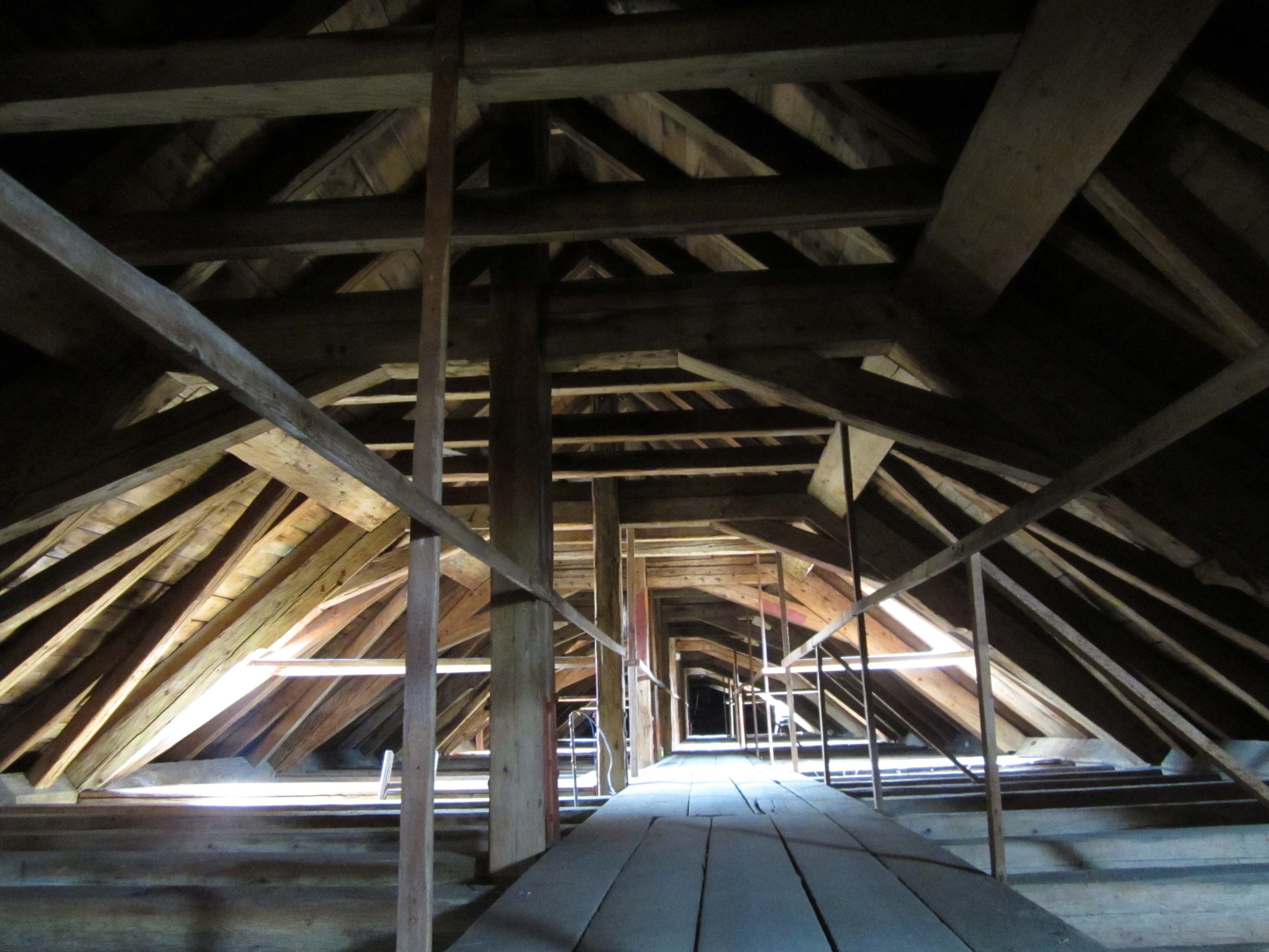 Einblick in den Dachraum des Stiftsgebäudes, dicke Holzbalken bilden den Dachstuhl, Dachfenster lassen etwas Tageslicht in den sonst dunklen und verstaubten Dachboden