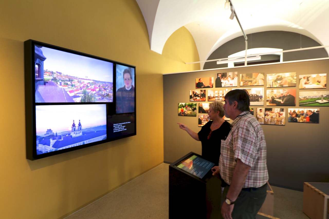 Zwei BesucherInnen stehen am Info-Point und erkundigen sich am großen Wanddisplay über das Stift Kremsmünster