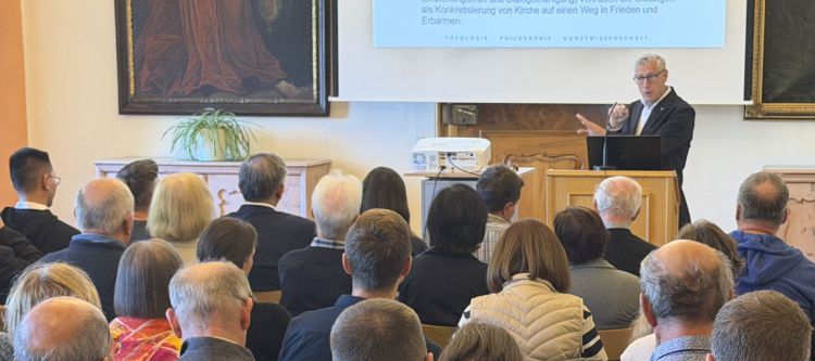 Porträt von Professor Volgger bei Vortrag, im Hintergrund Schrift auf eine Leinwand projeziert