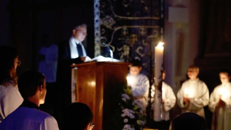 Kirche im Dunklen mit Kerzenschein, Priester am Ambo und Mininstranten