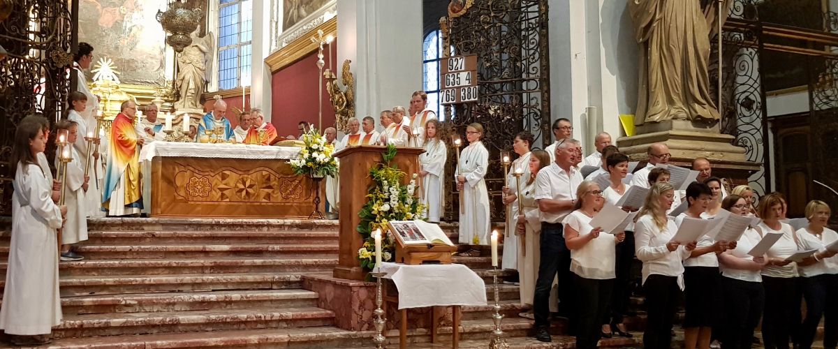 Gottesdienst in der Stiftskirche: Am Altar feiern festlich bekleidete Mönche und viele junge Ministranten die Eucharistie. Ein Chor hat sich aufgestellt, um gemeinsam zu singen.