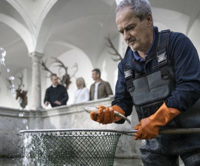 Ein Mann mit wasserfester Kleidung steht in einem Wasserbecken mit Kescher und einem Fisch in der Hand