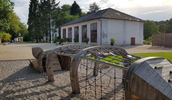 Ein Kinderspielplatz mit Klettergerüst in Form eines Wildschweines. Dahinter das Feigenhaus mit seinen fünf hohen Fenstern.