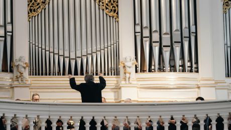 Orgelprospekt mit Orgelpfeifen und Dirigent mit Rücken im Bild dirigiert Richtung Orgel und Chor