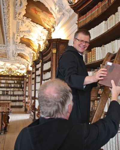 In der Stiftsbibliothek wählen zwei Mönche ein Buch aus den reich gefüllten Regalen