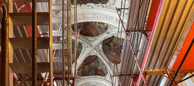 rotes Baugerüst im Inneren einer Kirche, nach oben hin Blick auf Stuck und Fresken