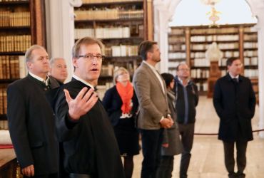 Ein Mönch steht mit mehreren Besuchern in der Stiftsbibliothek und gibt Erklärungen ab.