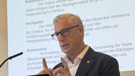 Porträt von Professor Volgger bei Vortrag, im Hintergrund Schrift auf eine Leinwand projeziert