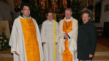 vier personen, davon zwei männer mit weiß-gelbem Priestergewand, eine Frau mit weißem Messgewand, ein Mann mit grauer Hose und schwarzer Jacke