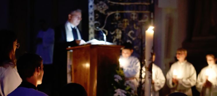 Kirche im Dunklen mit Kerzenschein, Priester am Ambo und Mininstranten