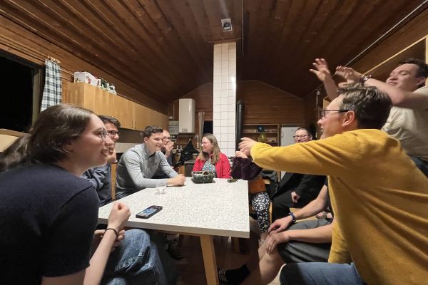 Spiel und Spaß in einer Hütte beim Almseewochenende. Junge Männer und Frauen sitzen im Kreis und diskutieren aufgeweckt und voller Freude