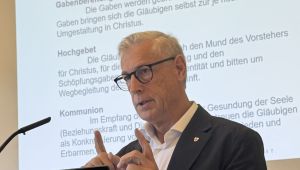 Porträt von Professor Volgger bei Vortrag, im Hintergrund Schrift auf eine Leinwand projeziert