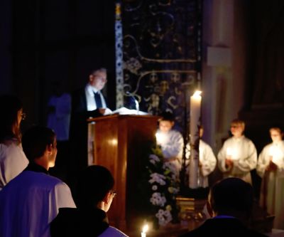 Kirche im Dunklen mit Kerzenschein, Priester am Ambo und Mininstranten