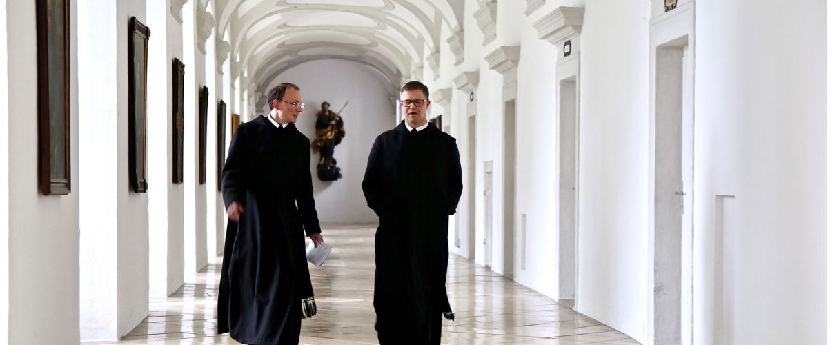 Zwei Mönche unterhalten sich beim gemeinsamen Spaziergang im Stiftsflur