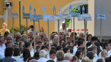 viele menschen halten Tafeln mit Kichenmodellen aus Metall, auf jeder steht der Name einer Pfarrkirche