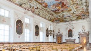 großer barocker Festsaal mit Deckenfresko und Stuck an den Wänden, mit aufgestellten Stühlen
