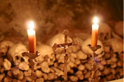 Jesuskreuz mit zwei Kerzen. Im Hintergrund, Totenköpfe.