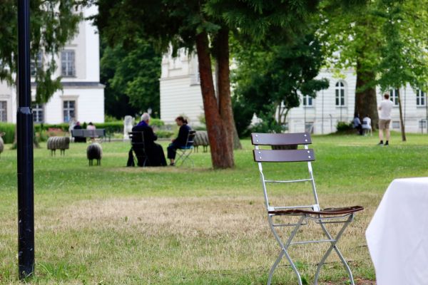 Auf der Wiese der Stiftsgärten werden vereinzelt Beichtgespräche abgehalten. Ein leerer Stuhl im Bildvordergrund lädt zur Seelsorge ein.