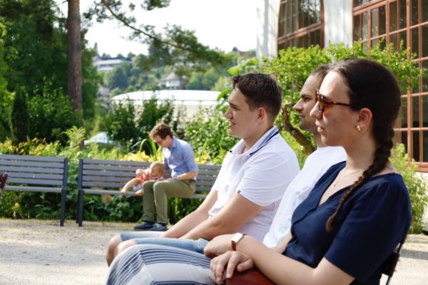 Portraitaufnahme von drei ZuhörerInnen beim Sommerfest. Im Hintergrund sitzen ein Vater und seine kleine Tochter auf der Parkbank.