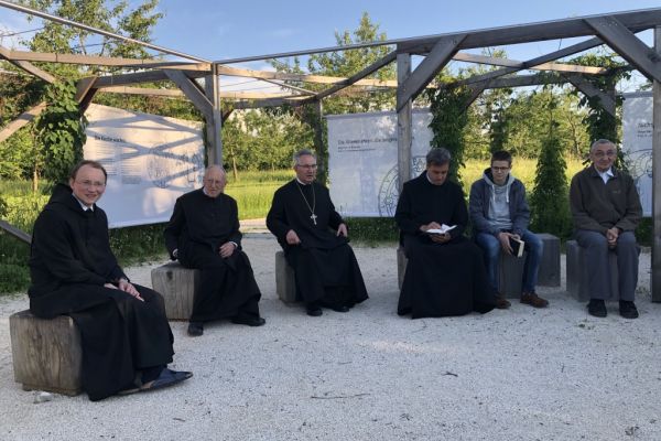 Mönche und Besucher im Freien, jeweils auf massivem Holzklotz sitzend