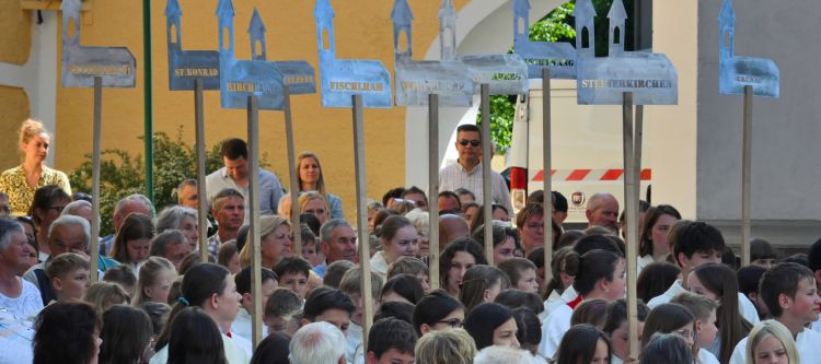 viele menschen halten Tafeln mit Kichenmodellen aus Metall, auf jeder steht der Name einer Pfarrkirche