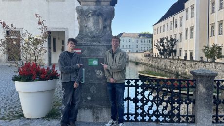 Zwei Schüler vor einem Wassergraben zeigen auf einen QR-Code