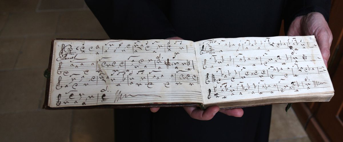 Ein Mönch gewährt einen Einblick in ein Notenbuch, welches per Hand beschriftet wurde