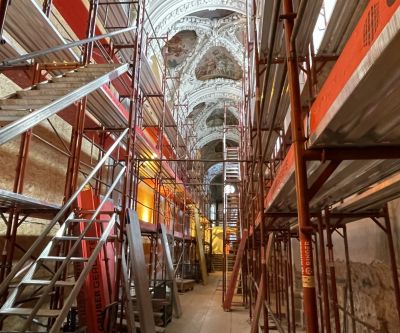 rotes Baugerüst im Inneren einer Kirche, nach oben hin Blick auf Stuck und Fresken