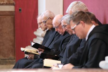 Mehrere Mönche sitzen andächtig in der Stiftskirche und beten gemeinsam mit Blick in deren Gebetsücher