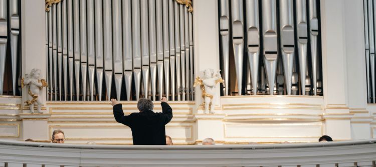 Orgelprospekt mit Orgelpfeifen und Dirigent mit Rücken im Bild dirigiert Richtung Orgel und Chor