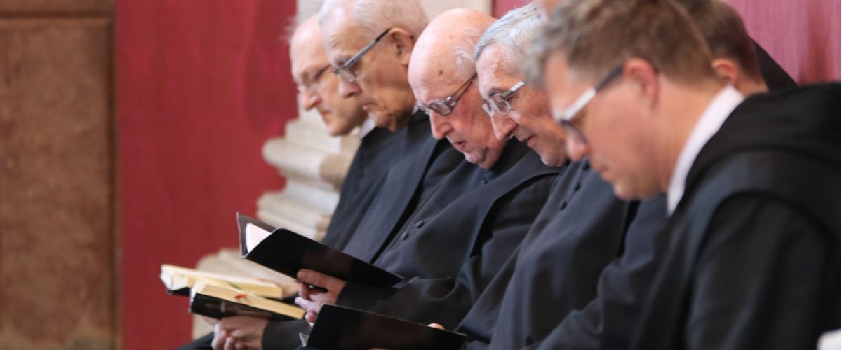 Mehrere Mönche blicken in deren Gebetsbücher und beten