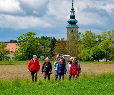 Kleine Pilgergruppe auf Wiesenweg mit Kirche im Hintergrund