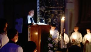 Kirche im Dunklen mit Kerzenschein, Priester am Ambo und Mininstranten