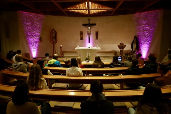 Heilige Messe im Haus Subiaco. Runde sitzbänke kreisen um das zentrale Kruzifix. Violette LED-Scheinwerfer schaffen ein passende Atmosphere zur Adventzeit.
