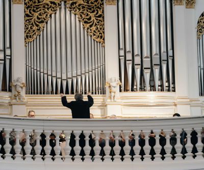 Orgelprospekt mit Orgelpfeifen und Dirigent mit Rücken im Bild dirigiert Richtung Orgel und Chor