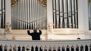 Orgelprospekt mit Orgelpfeifen und Dirigent mit Rücken im Bild dirigiert Richtung Orgel und Chor