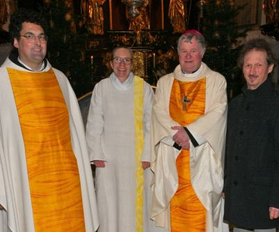 vier personen, davon zwei männer mit weiß-gelbem Priestergewand, eine Frau mit weißem Messgewand, ein Mann mit grauer Hose und schwarzer Jacke