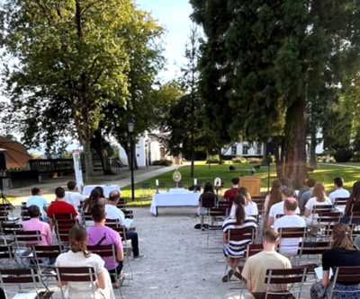 Junge Christen sitzen in Richtung aller Heiligstes im Stiftsgarten und warten auf den Beginn der heiligen Messe.