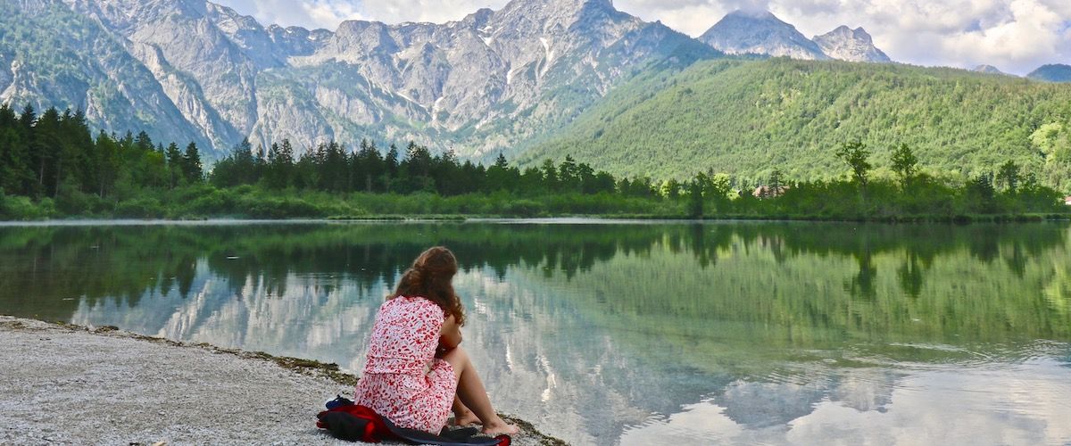 Person sitzt am Ufer des Almsees mit den Bergen im Hintergrund