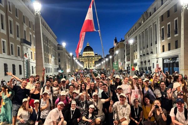 Großes Gruppenfoto vom Treffpunkt Benedikt: Voller Freude stehen und knien die Teilnehmer vor dem Petersdom in Rom und halten die Österreichfahne hoch in die Luft 