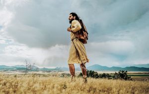 Jesus in einem Leinengewand und einem Lederrucksack um die Schulter in der Wüste, aus der Filmserie The Chosen